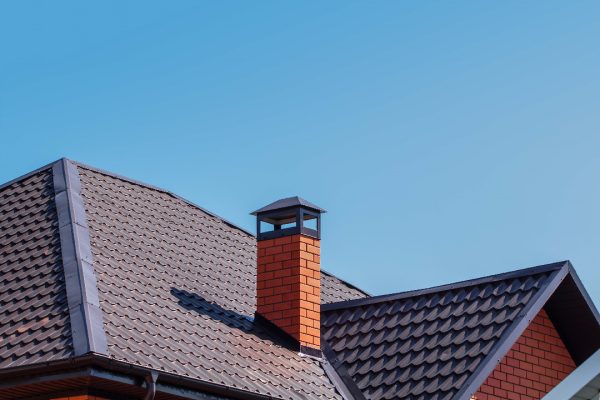 chimney The exterior of the roof of a country house against the sky. Brick chimney pipe on metal roof of a private house. Individual heating system. Rain gutter.